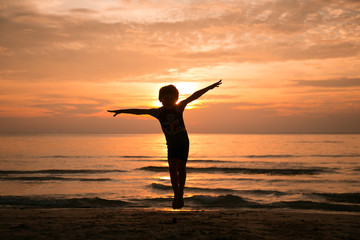 A boy jumps in the air arms to the sides at sunset on the sea