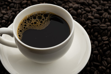 Hot black coffee with foam in a white coffee cup on coffee beans field background