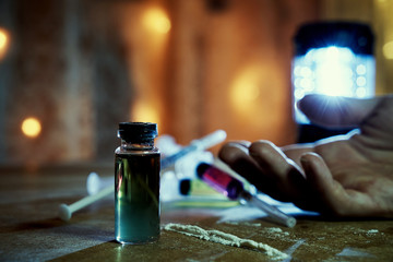 Drug overdose. The use of drugs leads to death. A bottle of heroin and a cocaine path near the hand of a dead man. Syringes with liquids in the bokeh