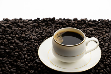 Hot black coffee with foam in a white coffee cup on coffee beans field background