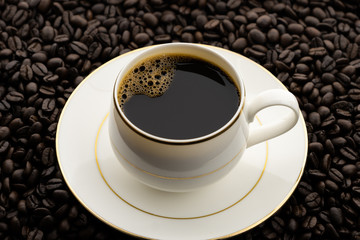 Hot black coffee with foam in a white coffee cup on coffee beans field background