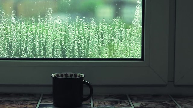 Hot cup of coffee is standing on the windowsill on the window background with raindrops.HD