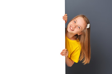 Funny teen girl in yellow clothes looks over a white wall, sign.