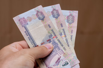 Persons hand giving the Currency of the United Arab Emirates (UAE) - Five hundred Dirham notes spread out on a brown background. Money exchange.