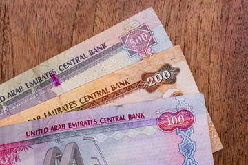 The Currency of the United Arab Emirates (UAE) - Close up of hundred Dirham notes on a brown table background. Money exchange.