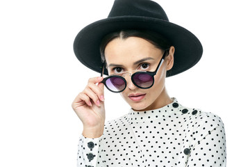 portrait of a girl with dark glasses in a black hat and a white polka dot dress on a white background
