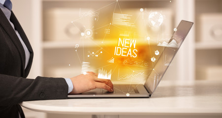 Side view of a business person working on laptop with NEW IDEAS inscription, modern business concept