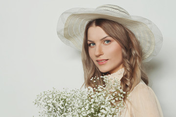 Cheerful blonde woman in hat holding flowers, close up portrait