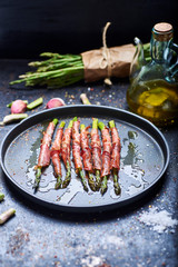 green asparagus with ham cooked on a black background and surrounded by ingredients.