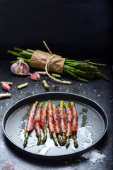green asparagus with ham cooked on a black background and surrounded by ingredients.