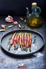 green asparagus with ham cooked on a black background and surrounded by ingredients.