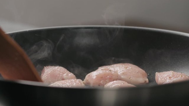 Slow motion moving chicken fillet slices on non-stick pan with wooden spatula closeup