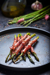 green asparagus with ham cooked on a black background and surrounded by ingredients.