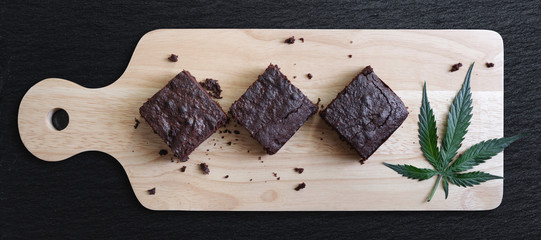Dark Chocolate Homemade Brownies Infused with Medical Cannabis, with Marijuana leaf on wooden tray