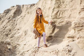 young woman in a yellow dress. little girl playing on the beach. young woman with teddy bear. Girl travels with her favorite toys.