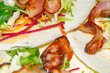 Leafy salad, sliced vegetables, sauce and fried bacon slices on pita bread are the basis for homemade Shawarma. Close up.