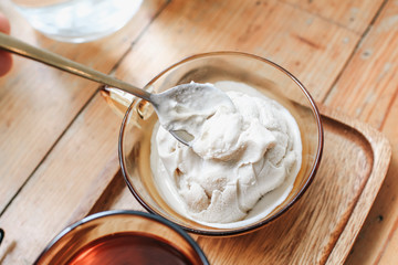 Using spoon eating brown cup with salted caramel ice cream and a glass of water on wooden vintage table.Cold dessert in cup. Business Breakfast. Sunny natural light enjoying holiday travel in cafe.