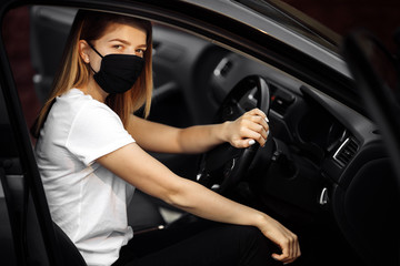 Fototapeta na wymiar Amazing young woman in a mask sitting in a car, protective mask against coronavirus, driver on a city street during a coronavirus outbreak, covid-19