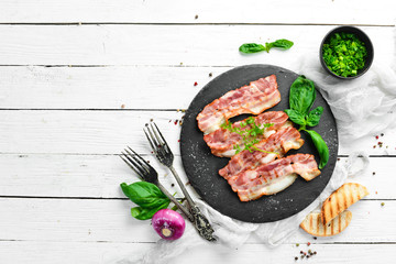 Fried bacon slices with basil on a black stone plate. Top view. Free copy space.