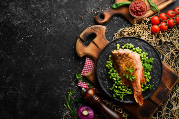 Baked sea red perch with green peas on a black stone plate. Top view. Free copy space.
