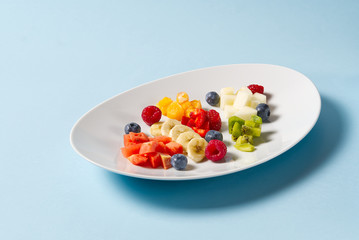Fresh fruit salad on white plate. Mixed fruit in white plate healthy food style. Useful fruit salad of fresh fruits and berries on light blue background