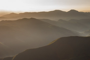 Fototapeta na wymiar Sunrise in the Pyrenees mountains. The ridges and ridges of the mountains in the misty morning haze at dawn. Incredible landscape on the path of Santiago. Hiking trail in spain. Way of Saint James.