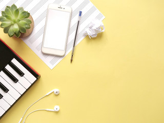 Top view of piano keyboard with sell phone, headphones, note paper and plant on yellow background. Study on smartphone, music online lesson, distance learning, hobby, home activity сoncept, copyspace