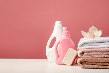 Stack of bath towels with white orchid flower, detergents and soap on pink background