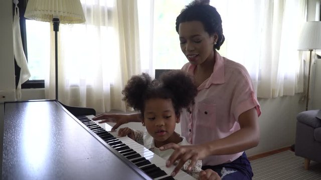 african american Mother playing piano with daughter in home . black mom with child.