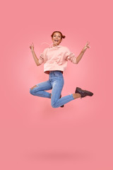 Full length shot of happy cheerful red-haired beautiful young girl in casual clothes jump in air on a pink background. Concept of happy news and promotions for youth. Advertising space