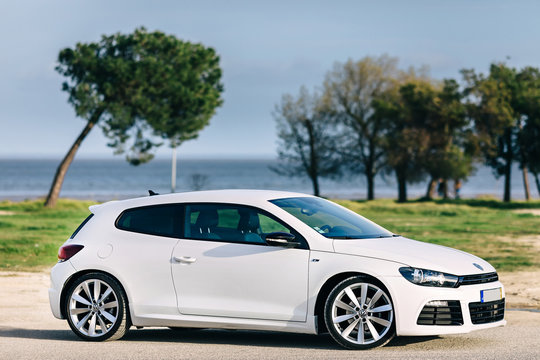 White sport hatchback parked on road side with sea background