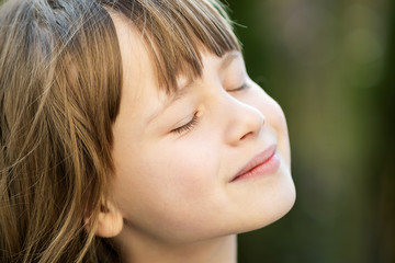 Portrait of young pretty child girl with long hair enjoying warm sunny day in summer outdoors. Cute female kid relaxing on fresh air outside.