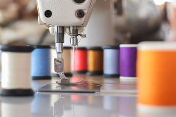 Needle presser foot of industrial sewing machine for sew cloth with colorful thread roll close-up.