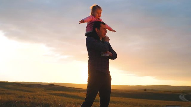 happy family. son sits on his neck teamwork at father shows hands to the side plays at the pilot depicts an airplane silhouette at lifestyle sunset. happy family concept childhood man dad with little