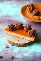 Almond tart with apricot jelly and whipped chocolate ganache, on a wooden board, on a bright blue and brown background.