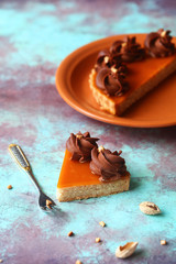 Almond tart with apricot jelly and whipped chocolate ganache, on a wooden board, on a bright blue and brown background.