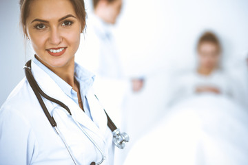 Female doctor smiling on the background with patient in the bed and two doctors