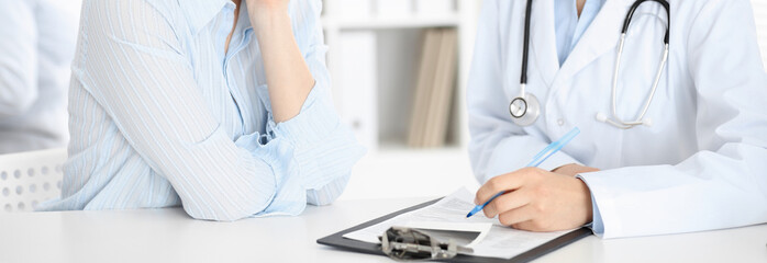 Unknown woman-doctor and patient sitting at the table. Very good news and high level medical service concept