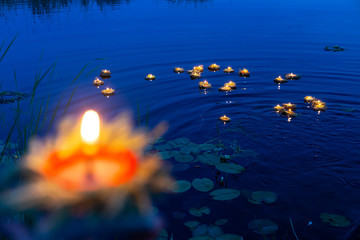 A hand holds a wreath and a fire on a Board close-up, a mysterious ancient Slavic pagan ritual, the light of lights on the lake in a blurred background