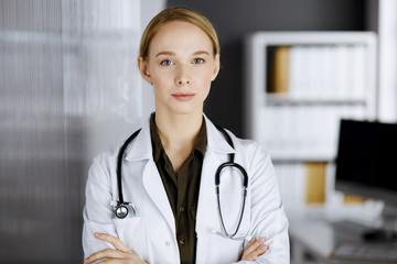 Friendly smiling female doctor standing in clinic. Portrait of friendly physician woman. Perfect medical service in hospital. Medicine concept