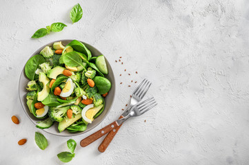 Avocado salad with boiled eggs, broccoli, spinach and almond nuts in bowl on white background. Top...