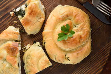 Traditional Balkan food, Serbian burek with cheese ans spinach, banica, Turkish borek on wood plate top view.