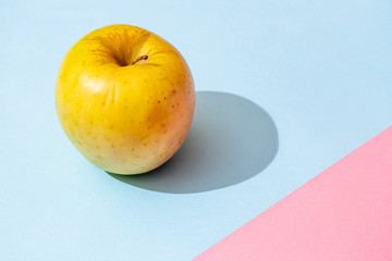 Yellow apple on pink blue background with hard shadow