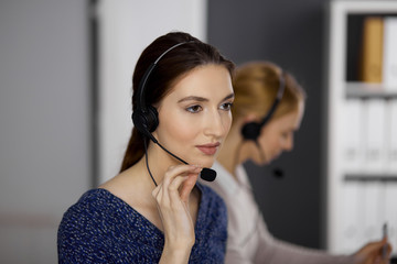 Friendly asian or Latin american businesswoman talking by headset in office. Call center and diverse people group in business