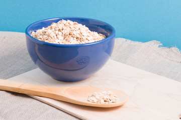 bowl of  dry oatmeal and wooden spoon on blue background 