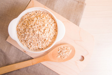  white bowl with a oatmeal and a large wooden spoon on a cutting board, light wooden table, yellow background, copy space, top view, natural linen fabric under a bowl