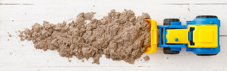 A boy plays with a large plastic tractor on a white wooden background. A tractor rakes kinetic sand. Early development for children. Wide view