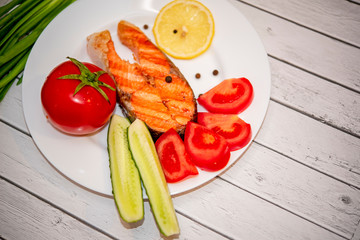 fried fish steak on a white plate with tomatoes, onions, cucumbers, on the boards