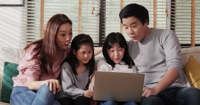 Little Girl And Her Parent Looking To Laptop Or Computer Together At Living Room. Happy Asian Family Laugh Look At Computer Screen Together Enjoy Do Internet Shopping.