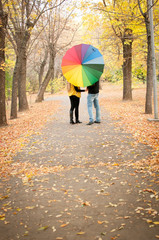 A young couple in love walks through the autumn Park holding hands. With a rainbow colored umbrella